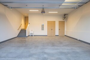 Amplio espacio interior bien iluminado, con suelo de hormigón, una escalera y dos puertas de madera.