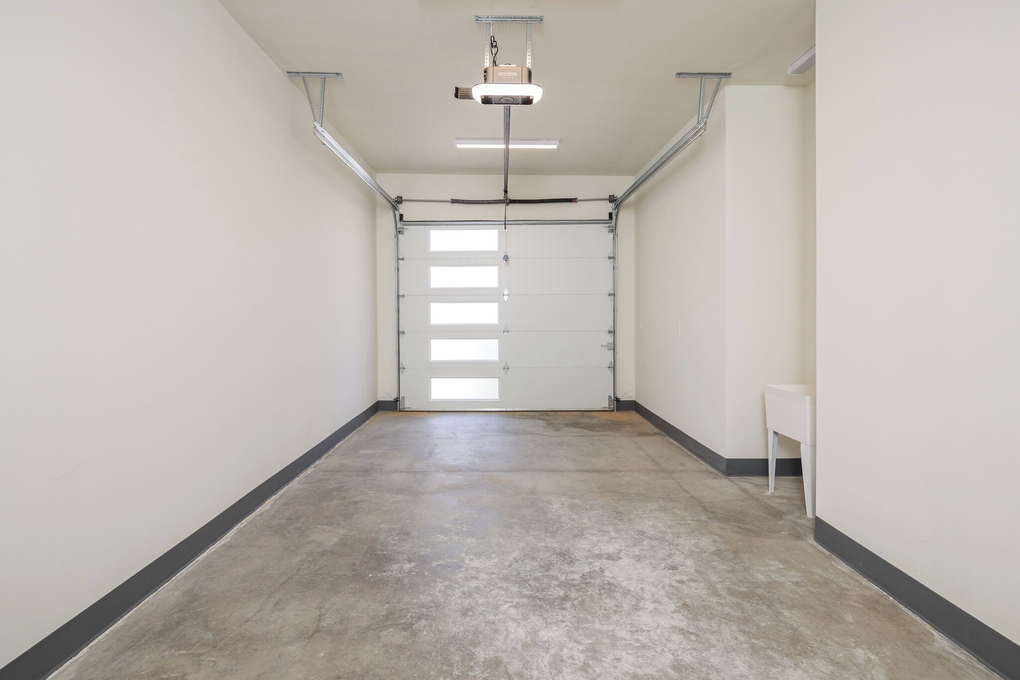 Un couloir doté d’un sol en béton, de murs blancs et d’une porte comportant plusieurs fenêtres.