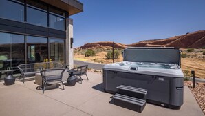 An outdoor patio with a hot tub, wicker furniture, and a view of red rock formations. - Lionsback Resort (Moab)