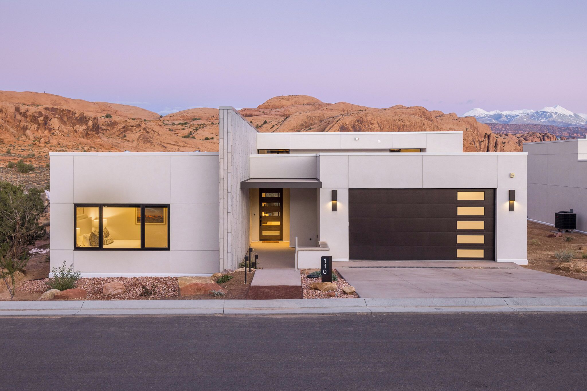 A modern two-story house with a garage, a well-maintained front yard, and a mountainous backdrop.