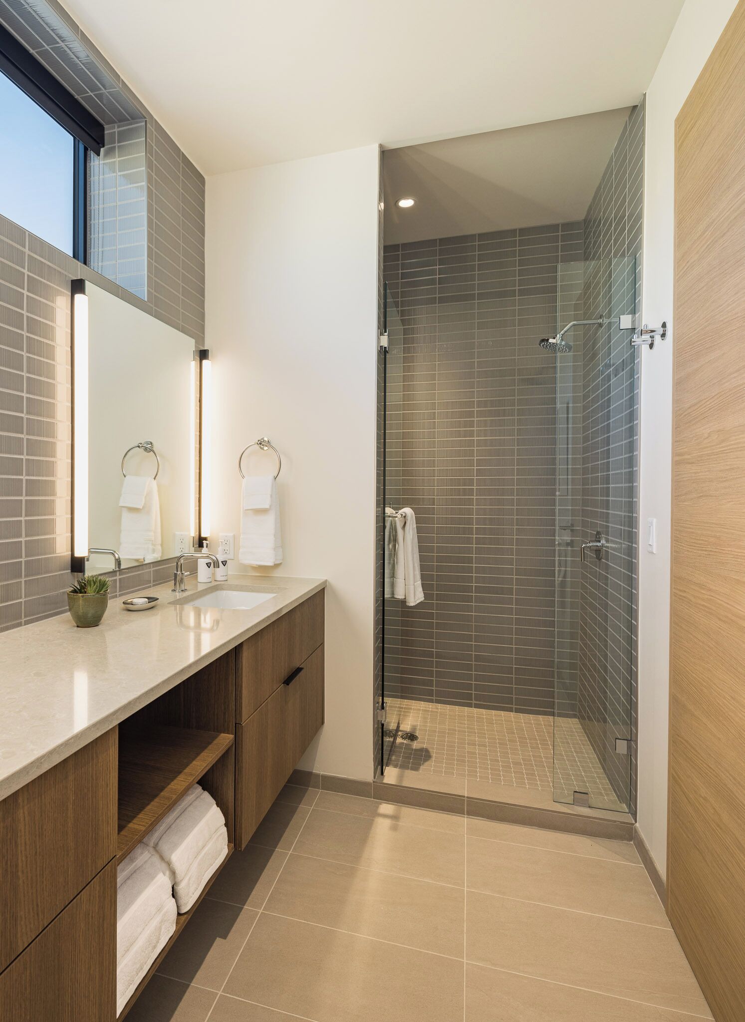 A modern bathroom with a glass-enclosed shower, a vanity with a mirror, and a window providing natural light.
