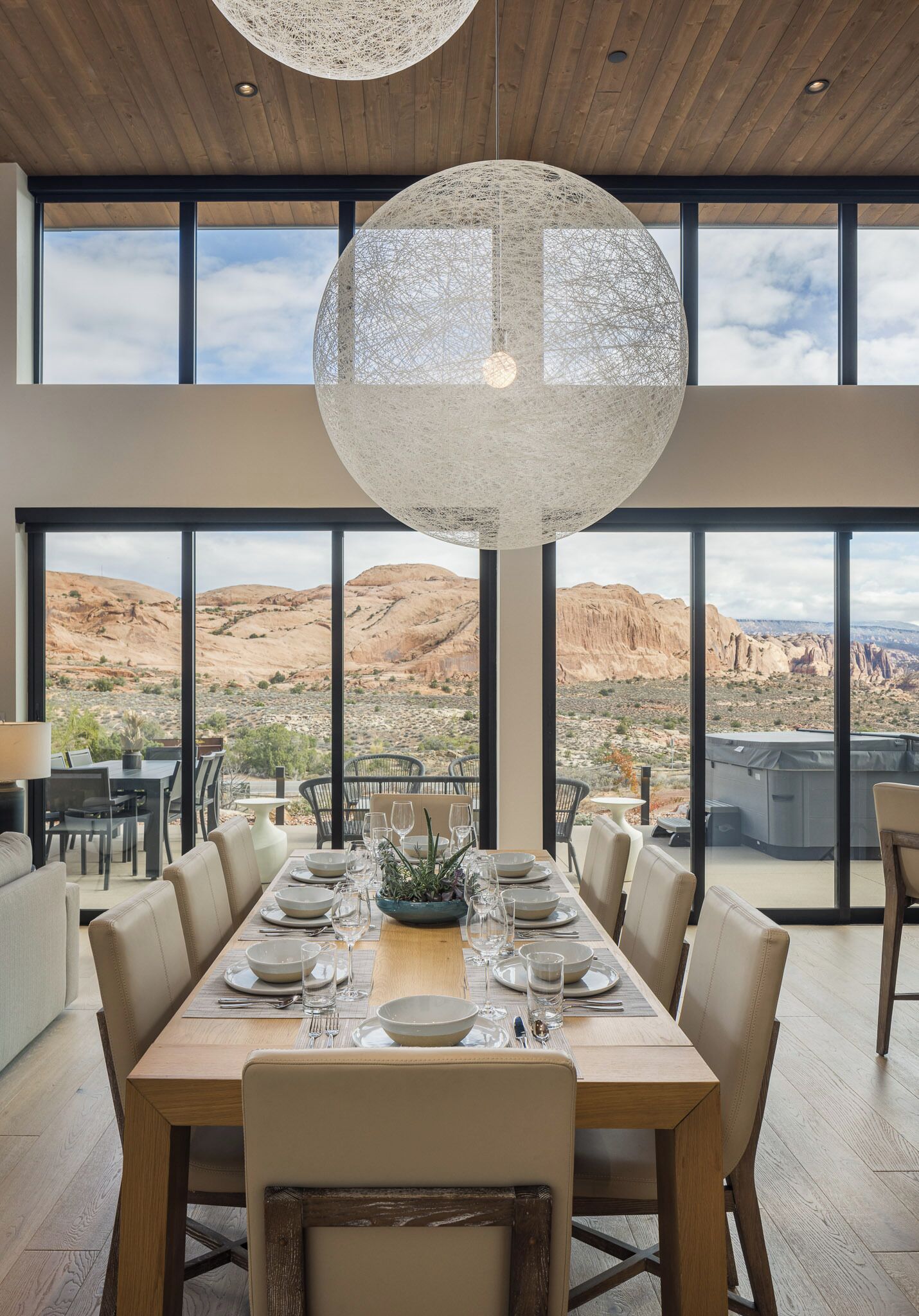 A dining area with a large table set for six, large windows offering a view of the desert landscape, and a hanging light fixture.