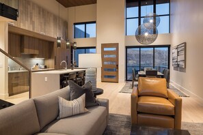 A spacious living area with a sofa, a leather chair, and a dining table. There is a kitchen with wooden cabinets and a large window overlooking a mountainous landscape. - Lionsback Resort (Moab)