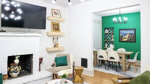 A modern living room with a flat-screen TV, fireplace, dining area, and green accent wall. - Exqusite Emerald (St. Louis)