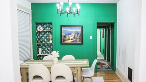 A dining area with a green wall, a wooden table, and white chairs. - Exqusite Emerald (St. Louis)