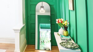A hallway with a green door, a white console table with a vase of flowers, and a hanging light fixture. - Exqusite Emerald (St. Louis)