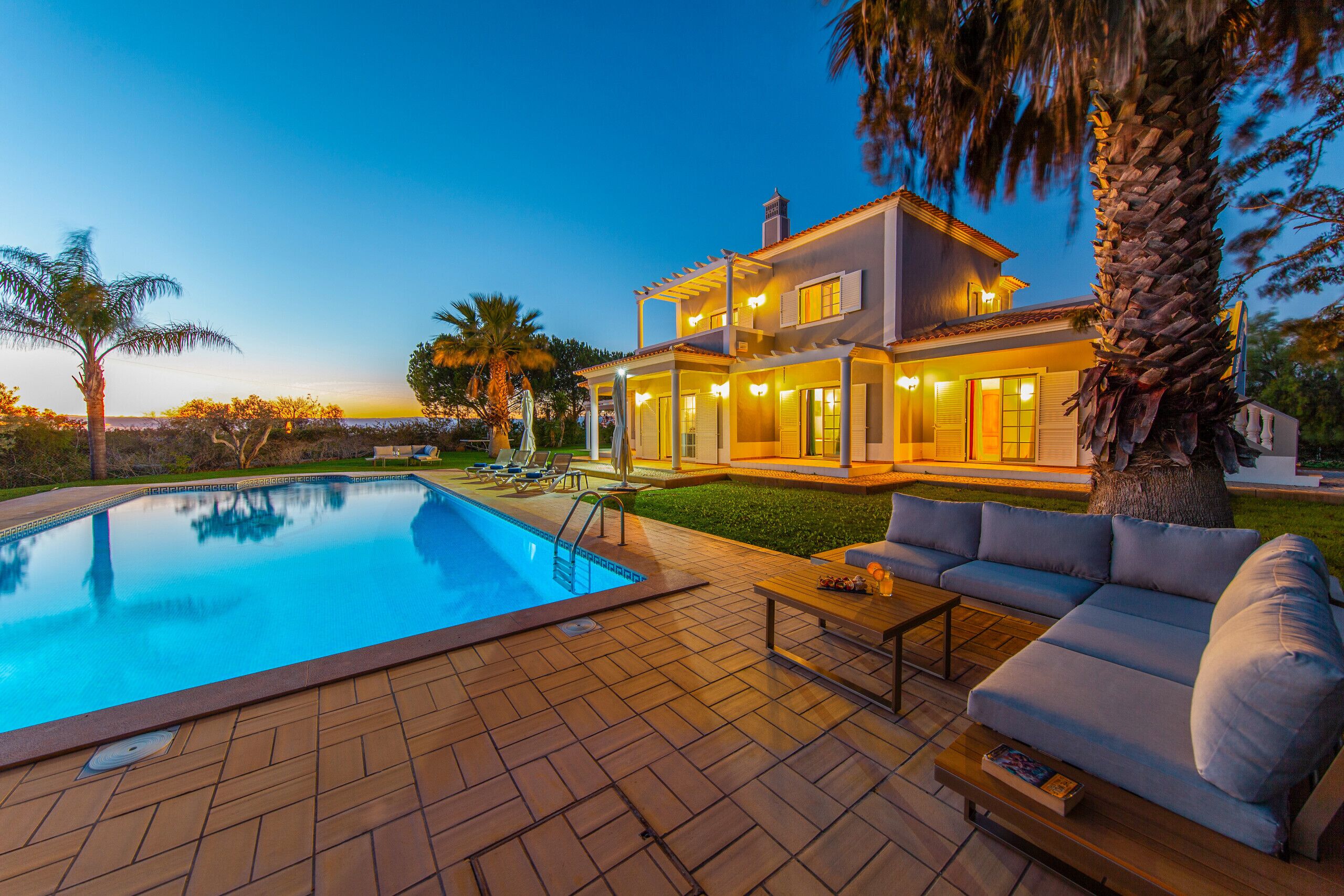 A two-story house with a swimming pool, outdoor seating, and a well-lit patio area.