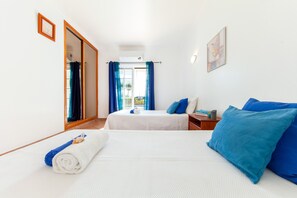 Een hotelkamer met twee bedden, een groot raam met gordijnen, een houten vloer en een kleine tafel met een lamp.