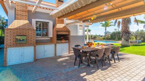 Une terrasse extérieure avec un barbecue en briques, une piscine et un espace salon abrité.
