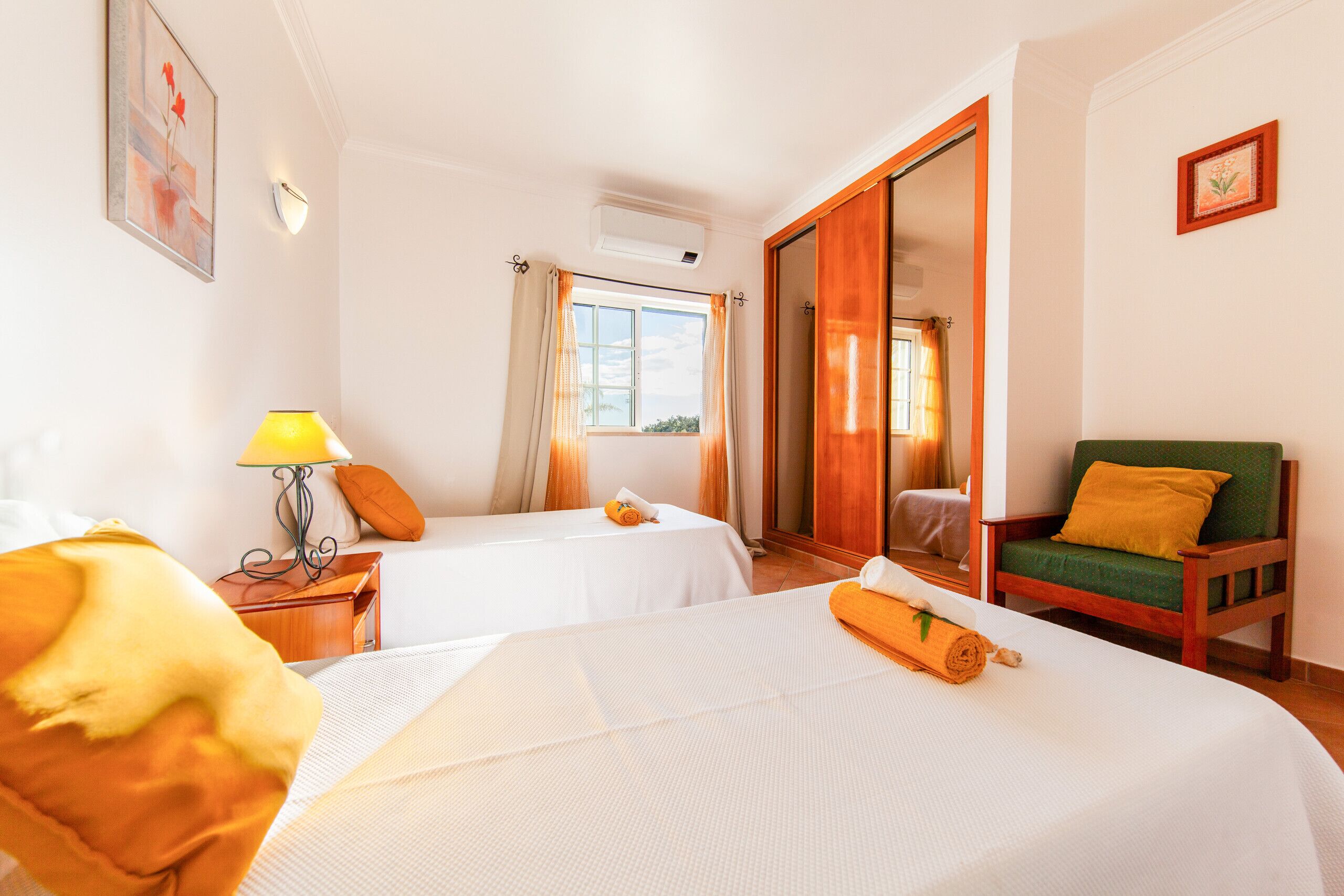 A hotel room with two beds, a wooden chair, a lamp, and a window with curtains.