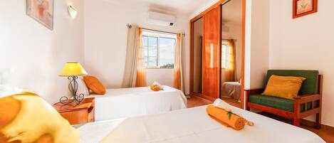 A hotel room with two beds, a wooden chair, a lamp, and a window with curtains.