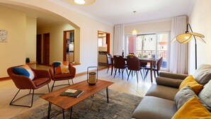 A modern living room with a sofa, armchairs, a coffee table, and a dining area with chairs and a table. - Apartment Niya (Loulé)
