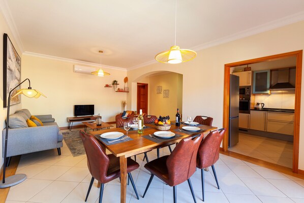 A modern living room with a sofa, TV, and dining area with a table set for four.