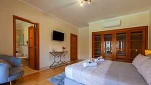 A bedroom with a large bed, a TV, wooden doors, and a small table with a plant. - Apartment Niya (Loulé)