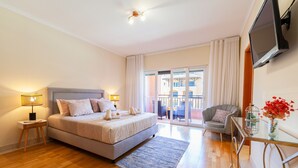 A modern hotel room with a bed, bedside lamps, a glass table with a vase, and a view of the outside balcony. - Apartment Niya (Loulé)