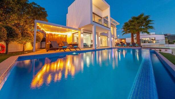 A modern two-story house with a swimming pool, outdoor seating, and a pergola with string lights. - Villa Catalina (Silves)