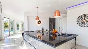 A modern kitchen with a large island, pendant lighting, and a clock on the wall. - Villa Catalina (Silves)