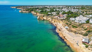 An aerial view of a coastal town with a beach, cliffs, and residential buildings. - Villa Catalina (Silves)
