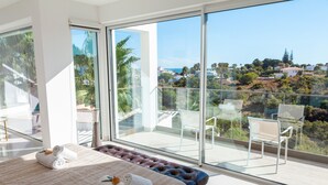 A bedroom with a large bed, a glass balcony, and a view of a hillside. - Villa Catalina (Silves)