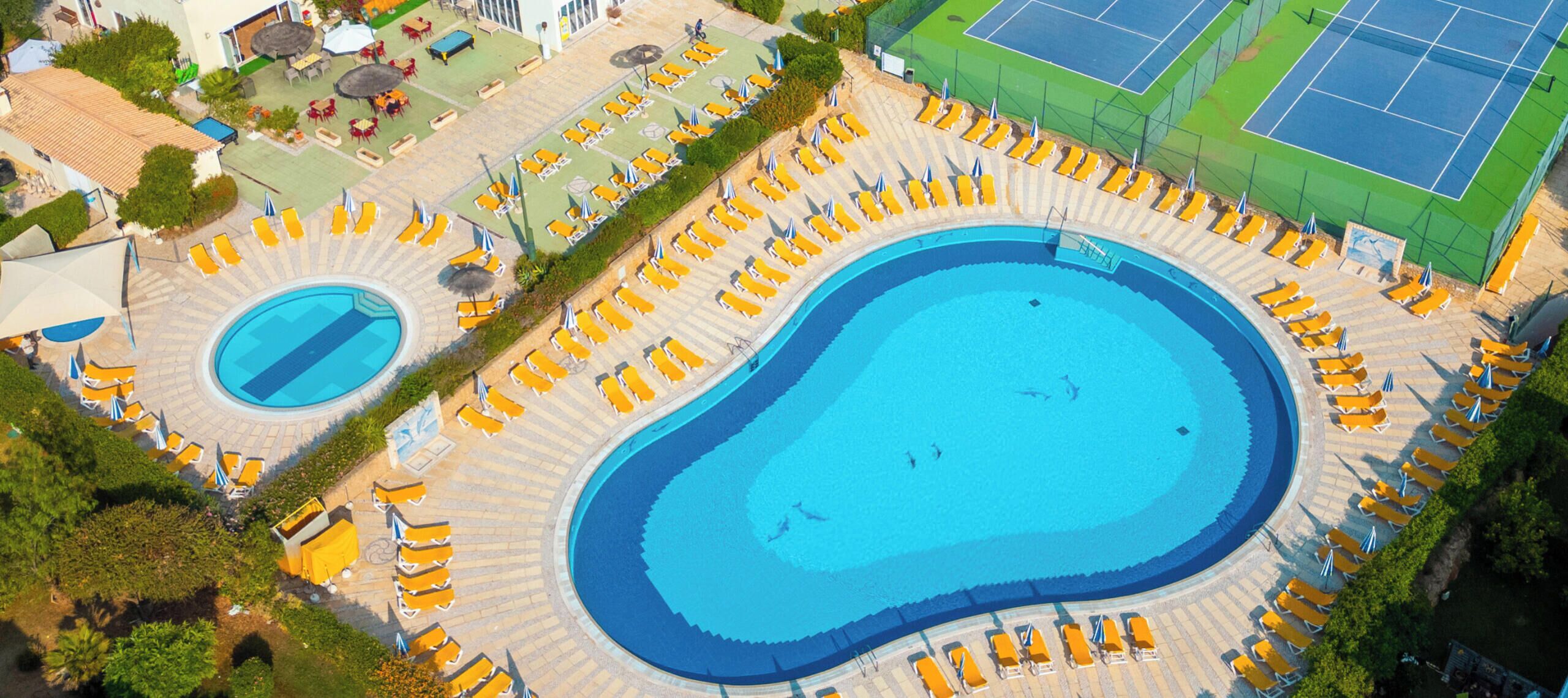 A resort with a large pool, tennis courts, and a building with a sustainability logo.