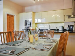 A dining table set with plates, cutlery, and wine glasses, with a kitchen in the background. - The Courtyard in the heart of Salcombe. (Salcombe)