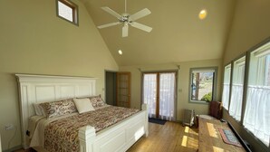 A bedroom with a large bed, a ceiling fan, a wooden dresser, and a view of the outdoors through the windows. - Charming farmhouse in Historic Spring City with AC, WiFi, and full kitchen. (Spring City)