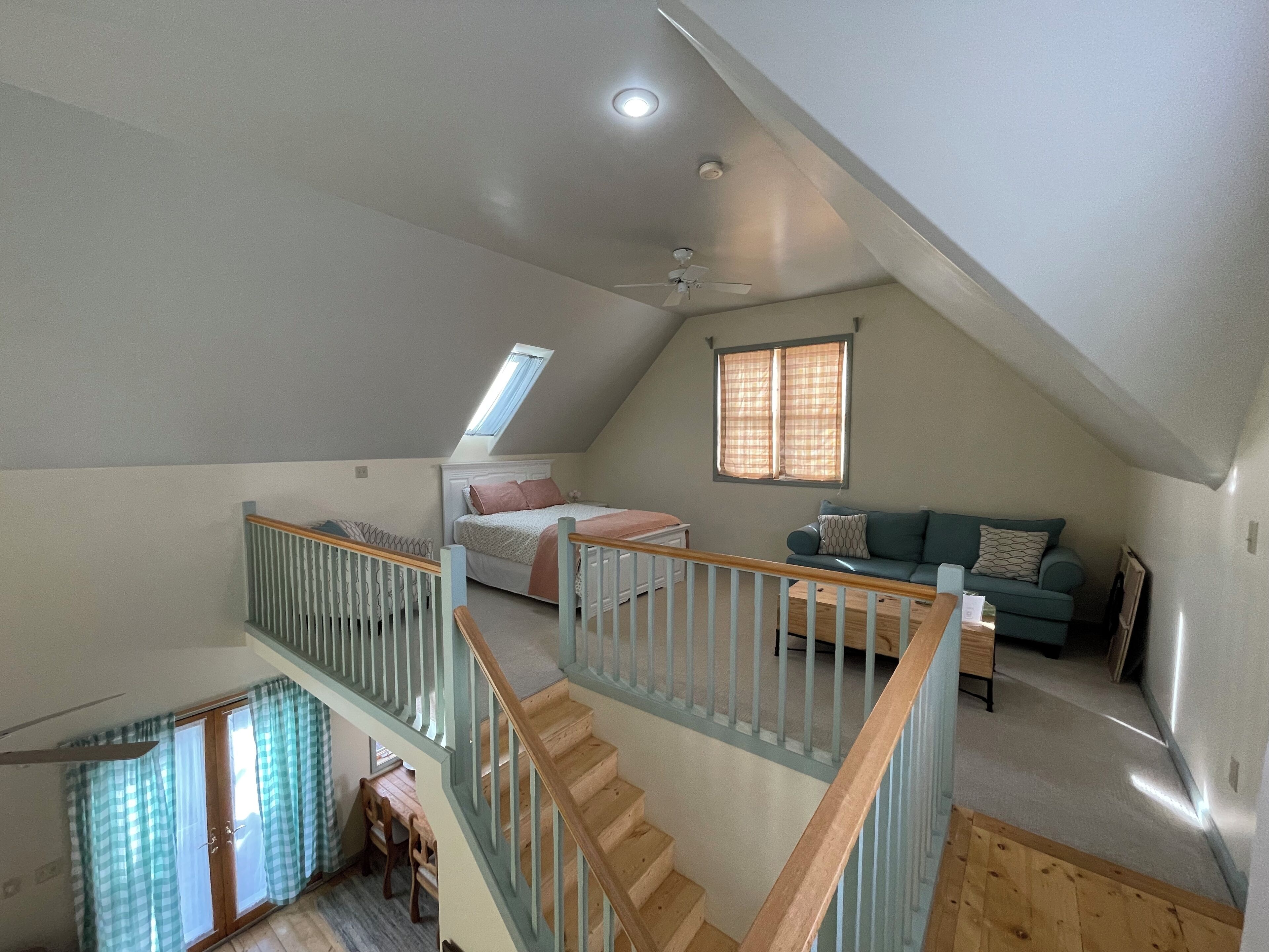 A loft bedroom with a sloped ceiling, a skylight, a bed, a sofa, and a staircase.