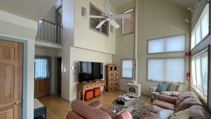 A spacious living room with a high ceiling, a television, a fireplace, and a large window. - Charming farmhouse in Historic Spring City with AC, WiFi, and full kitchen. (Spring City)
