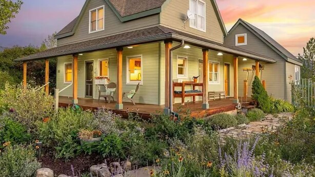 A two-story house with a porch, a covered front porch area, and a garden with various plants and flowers. - Charming farmhouse in Historic Spring City with AC, WiFi, and full kitchen. (Spring City)