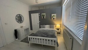A bedroom with a bed, bedside table, lamp, and a window with blinds. - Bed & Breakfast - 2 Double Rooms With Ensuites (Poole)