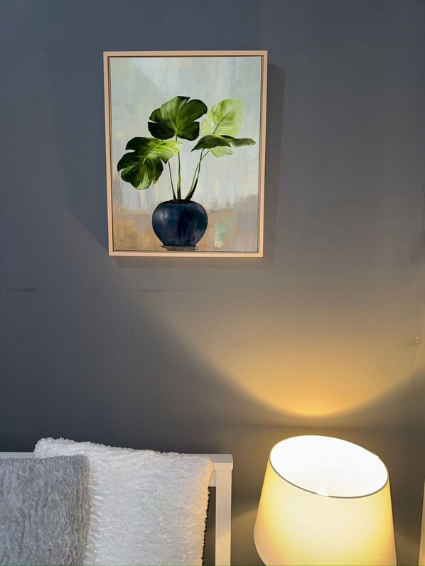 A framed painting of a potted plant on a wall, a white towel on a rack, and a lit lamp. - Bed & Breakfast - 2 Double Rooms With Ensuites (Poole)