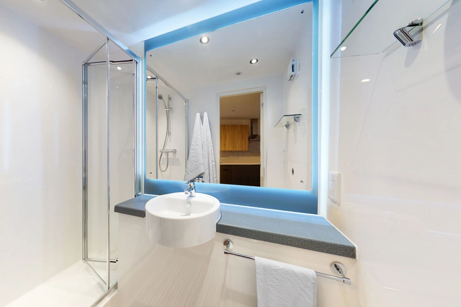 A modern bathroom with a glass shower enclosure, a white sink, and a large mirror.