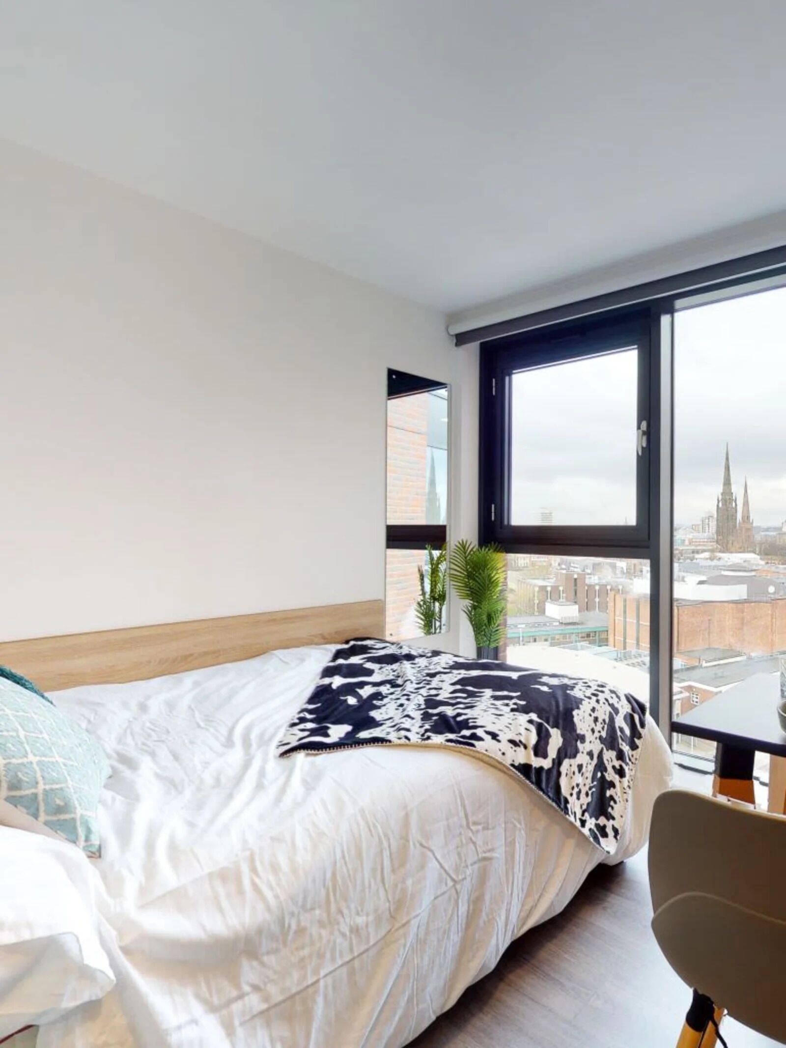 Un dormitorio moderno con un ventanal grande, una cama, una silla y una mesita.