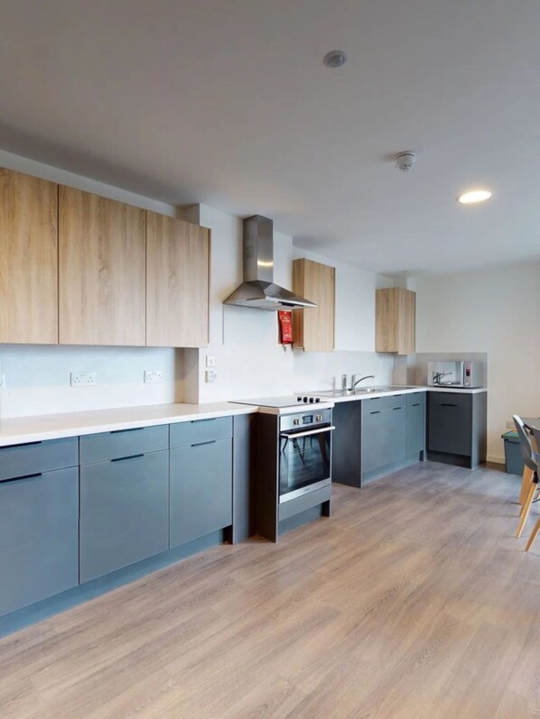 A modern kitchen with grey cabinets, a stainless steel range hood, and a built-in oven. - For Students Only Canvas Arundel House in Coventry (Coventry)