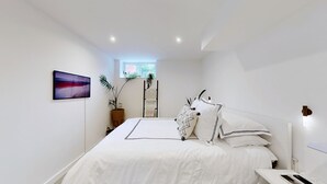Une chambre à coucher avec un lit, un tableau, une plante et une échelle appuyée contre le mur.