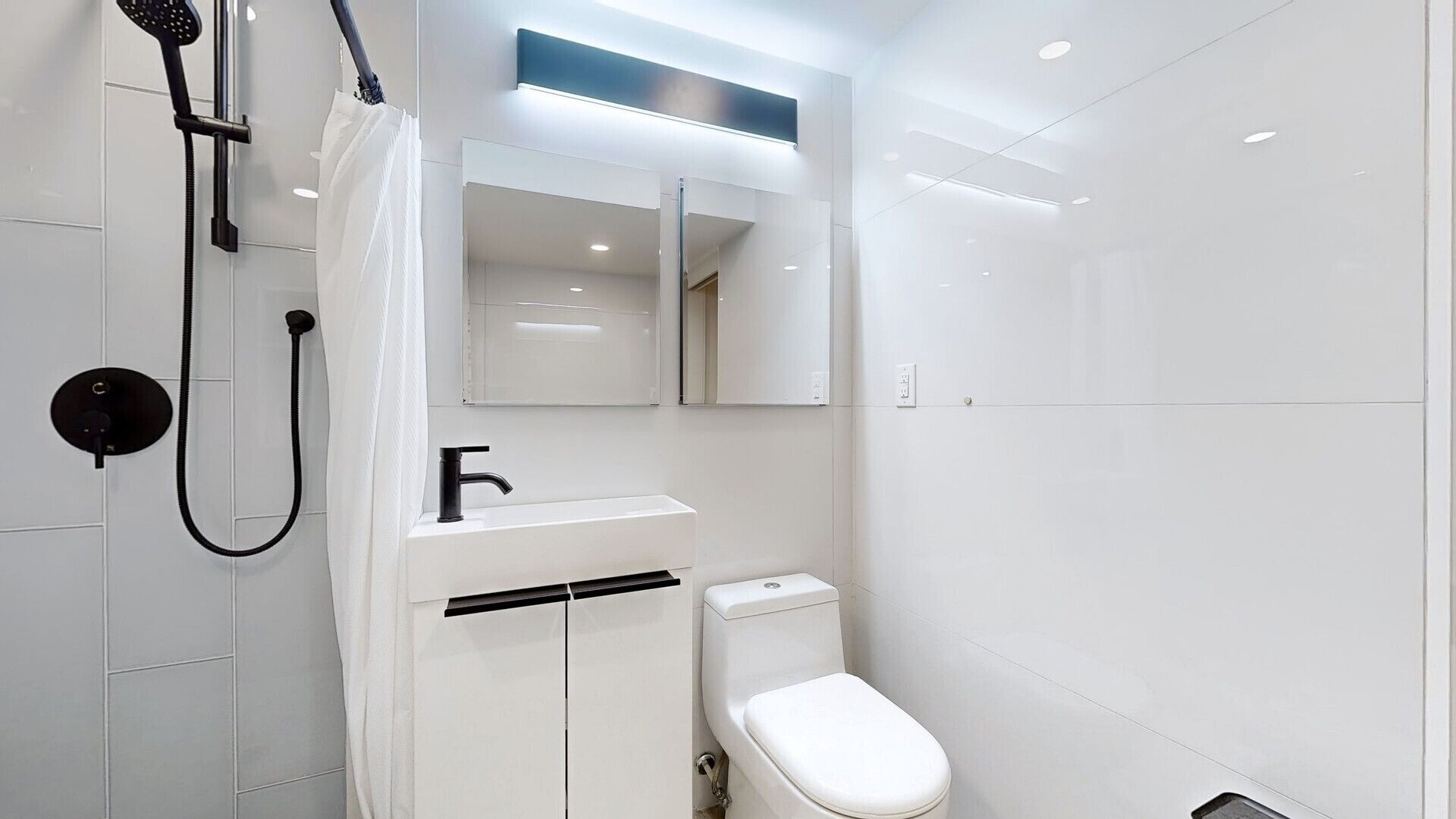 Un baño moderno con inodoro, ducha con cabezal de mano, toallero y espejo sobre el lavamanos.