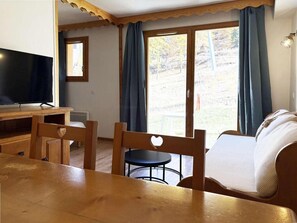 A room with a wooden table, chairs, a sofa, a television, and a sliding glass door leading to an outdoor area.