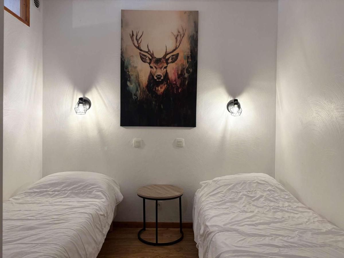 A room with two beds, a round table, and a painting of a deer on the wall.