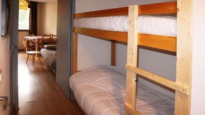 A bunk bed room with a wooden floor and a table with chairs in the background. - Resort center, 3rd floor, balcony, tv, ski locker, 28m², Les Orres (Les Orres)