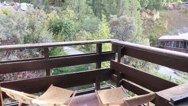A wooden deck with two wooden chairs and a view of a forested area with trees and a building in the background. - Resort center, 3rd floor, balcony, tv, ski locker, 28m², Les Orres (Les Orres)
