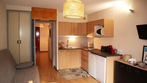 A compact living space with a kitchenette, a sofa, a small round table, and a television mounted on the wall. - Resort center, 3rd floor, balcony, tv, ski locker, 28m², Les Orres (Les Orres)