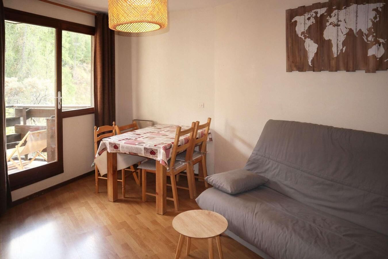 Un soggiorno accogliente con un divano grigio, un tavolo da pranzo in legno con sedie e una grande finestra vista alberi.