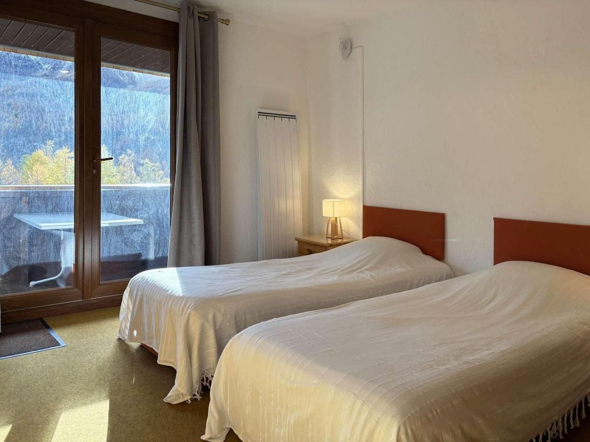 Ein Hotelzimmer mit zwei Betten, einer Schiebetür zu einem Balkon, einem kleinen Tisch und einer Lampe.