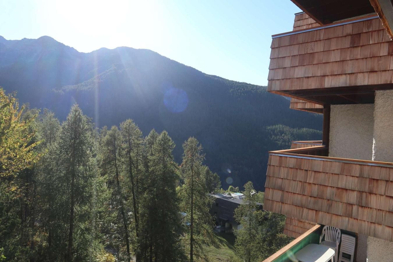 A mountain cabin with a wooden exterior and a balcony overlooking a forested valley.