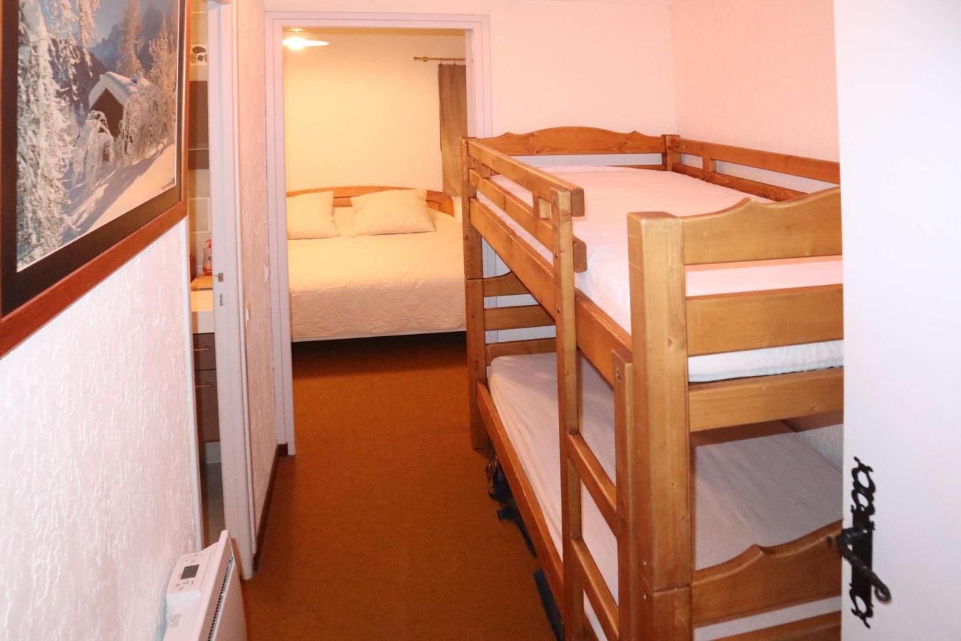 Une chambre avec deux lits superposés, une porte donnant sur une autre pièce et un tableau encadré au mur.