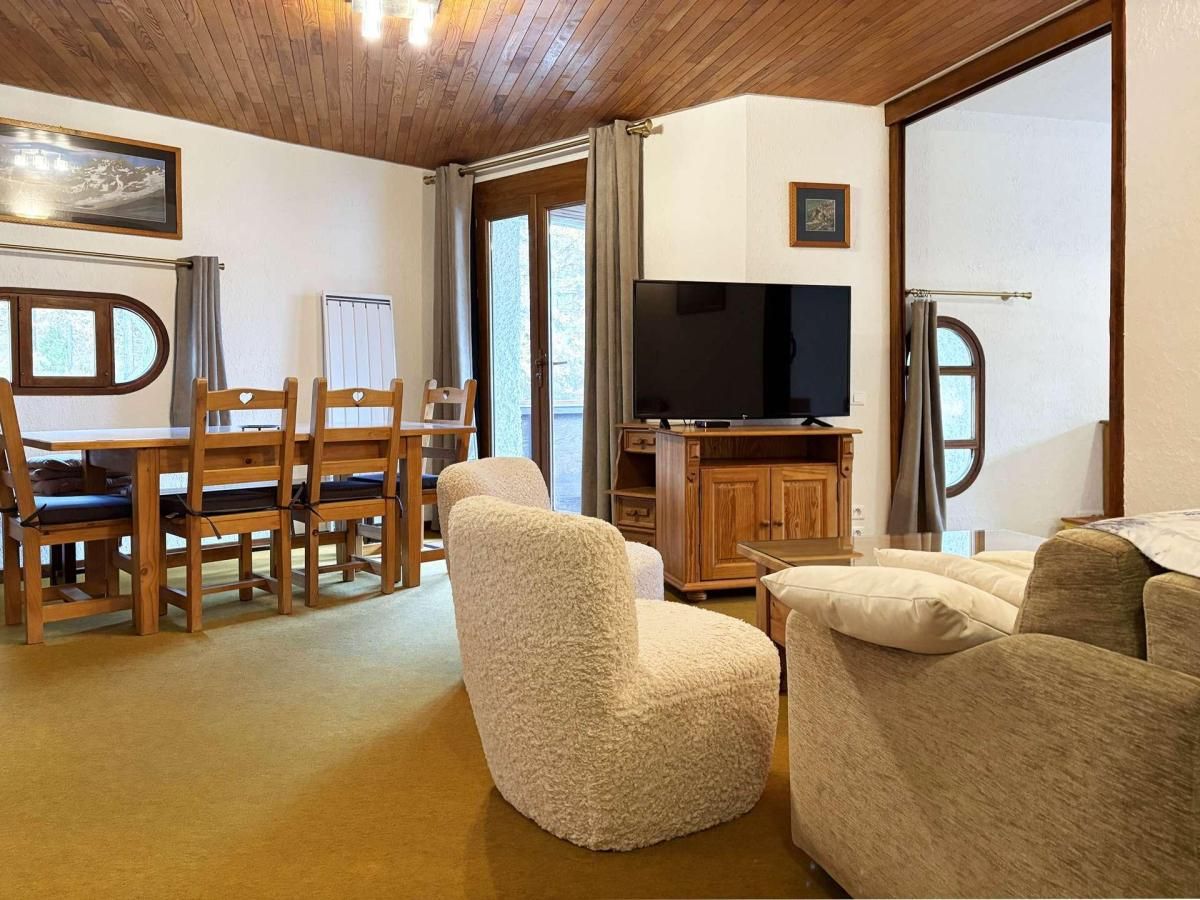 Ein gemütliches Wohnzimmer mit Holzesstisch, Stühlen, Fernseher und einer Couch.