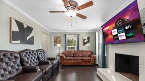 Un salon avec un canapé en cuir marron, un ventilateur de plafond et un téléviseur à écran plat diffusant des services de streaming.