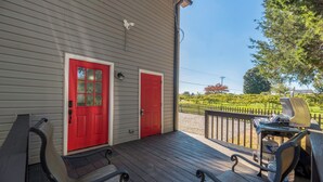 Une terrasse en bois avec deux portes rouges, un banc et un barbecue.