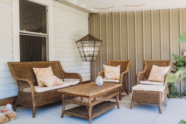 Relax in the covered porch's cozy seating area, featuring wicker chairs and a small table.