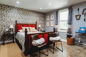 Classic bed with a patterned bedspread, complemented by a pair of leather chairs and a side table with a lamp.